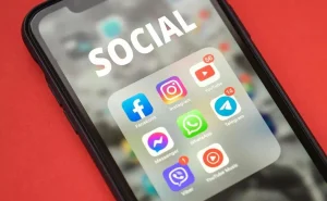 A imagem exibe um smartphone com a tela exibindo diversos aplicativos sociais, tais como Faebook, Instagram, YouTube; e também aplicativos de mensagem instantânea, como Whatsapp, Telegram, Viber; entre outros.