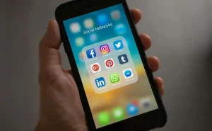 Smartphone exibindo uma lista de aplicativos de redes sociais, tais como Facebook, Instagram, Twitter, Pinterest, LinkedIn, e outros.